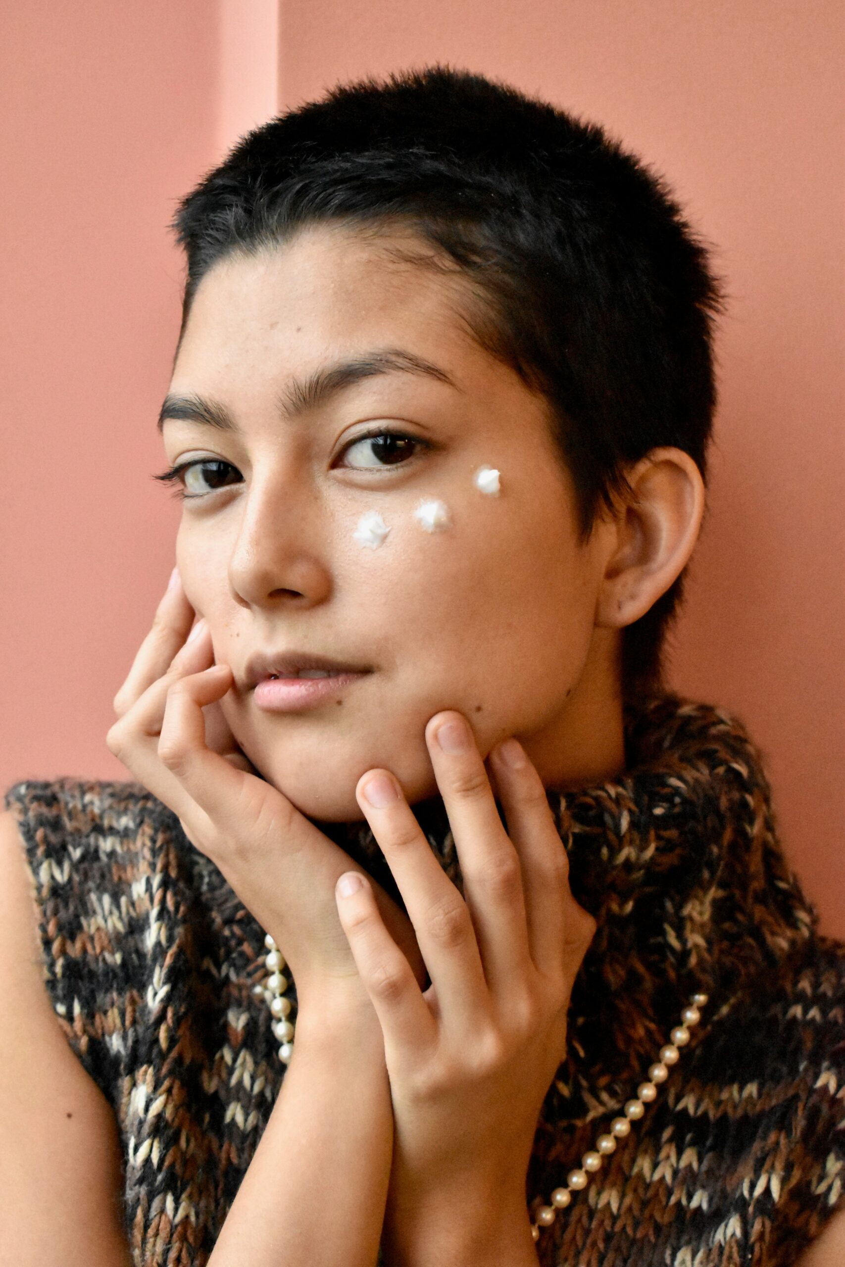 A woman applies skincare cream on her cheek.