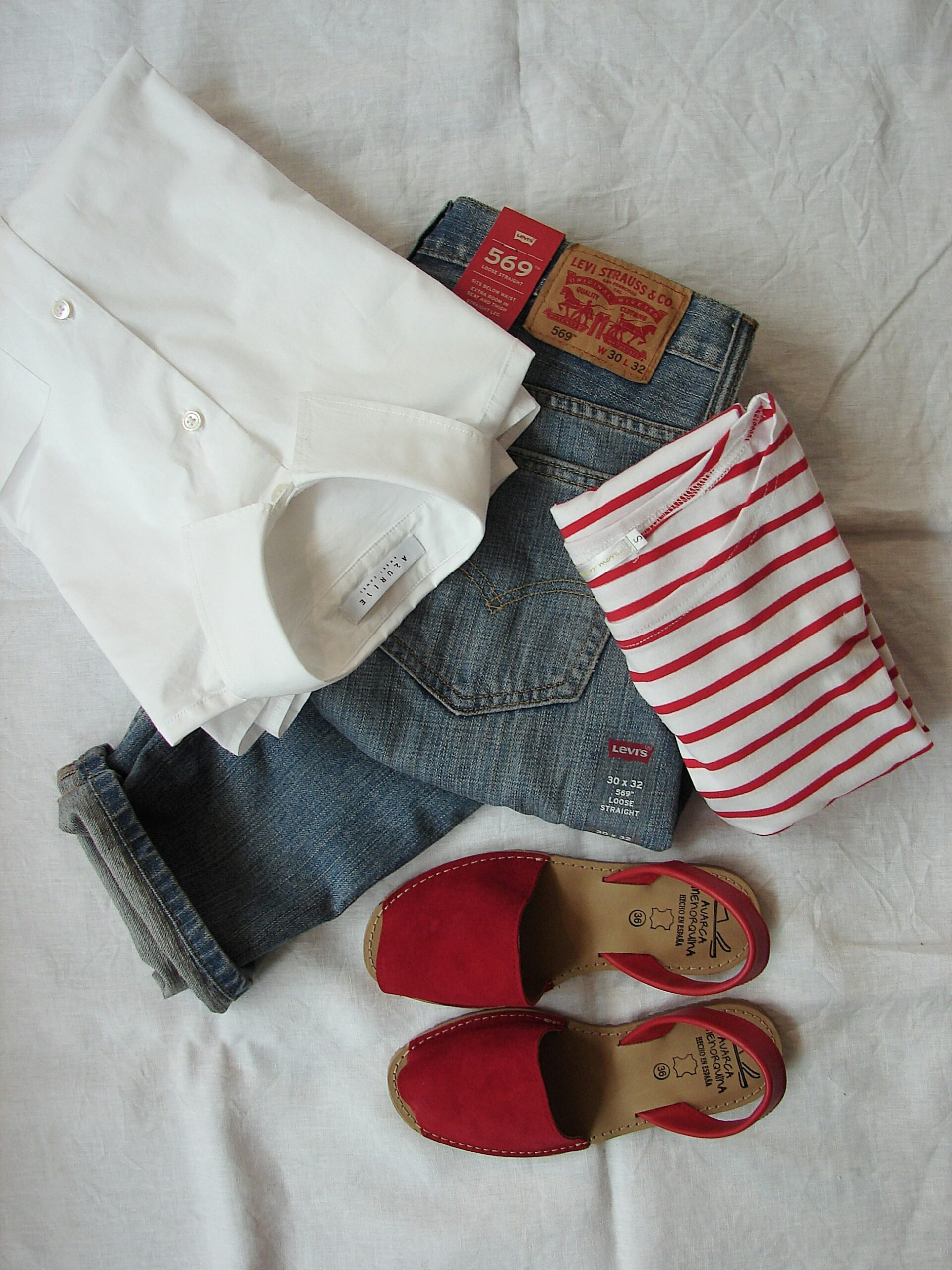 Flat lay of casual outfit with jeans, white shirt, striped top and red sandals — modern minimalist fashion styling, 2026 trends