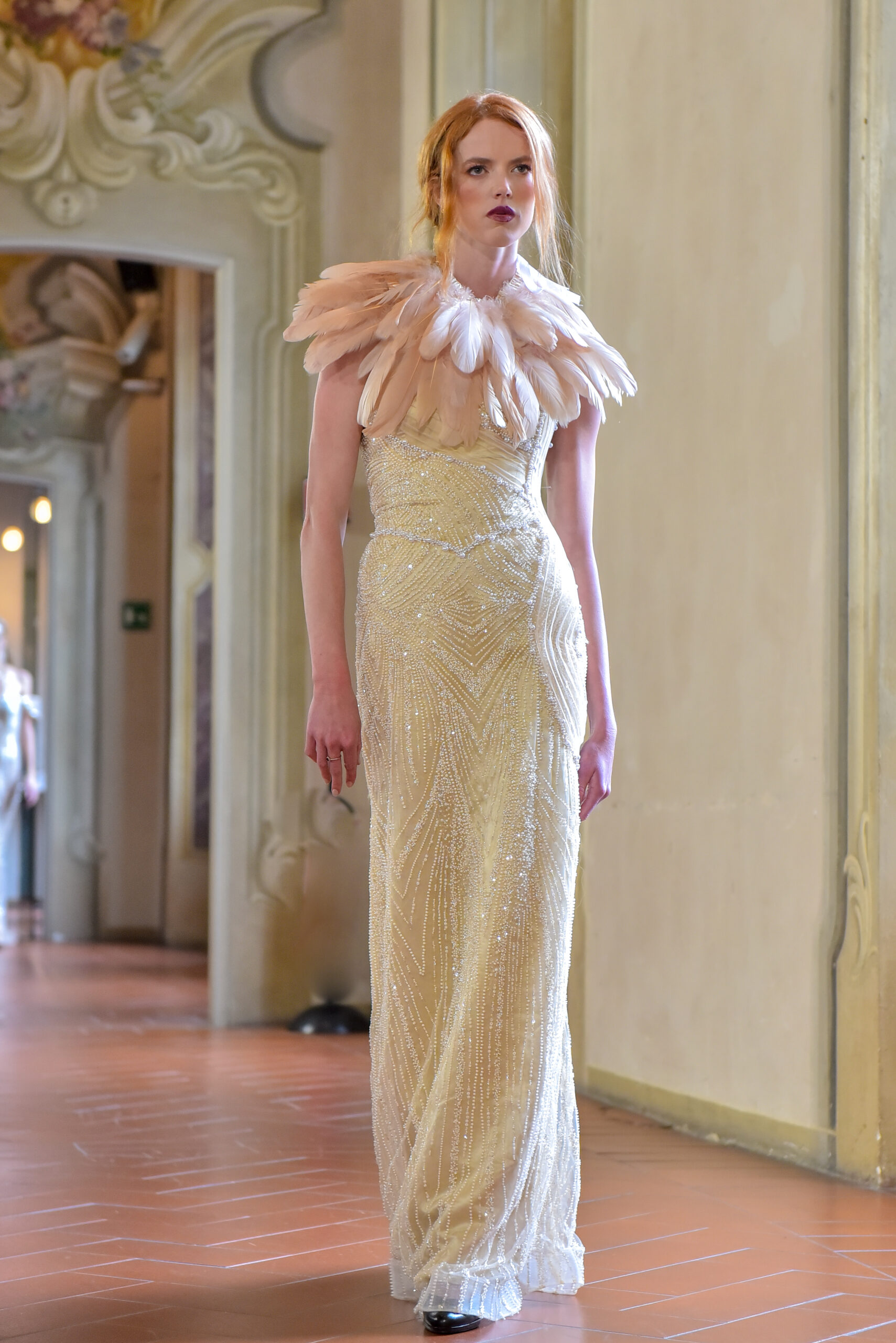 Model wearing a sculptural beaded couture gown with feather collar by Luxe Living Fashions at Centro Ambrosiano during Milan Women’s Fashion Week FW 2026–2027