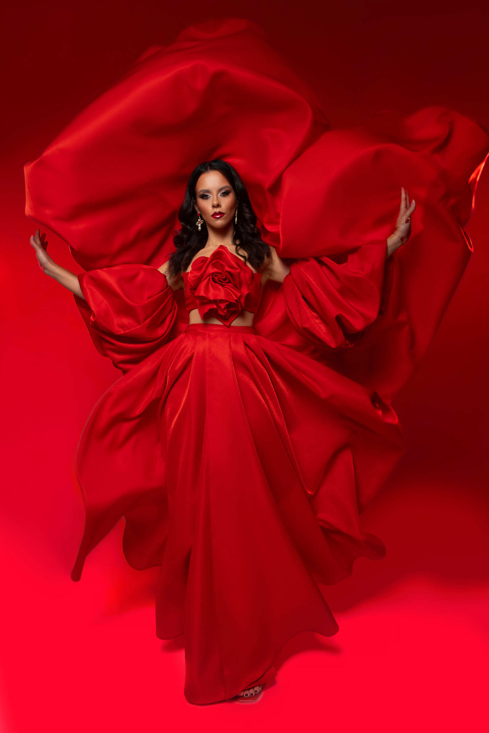 Model wearing a dramatic red couture gown by TutTrostyle with voluminous sculptural sleeves.