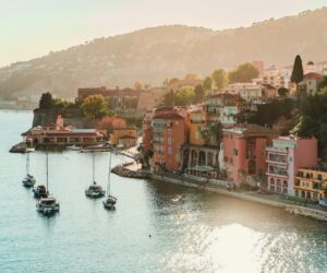 Sunlit view of St. Tropez on the French Riviera with pastel waterfront houses and luxury yachts, capturing the refined resort atmosphere associated with The White Lotus aesthetic.