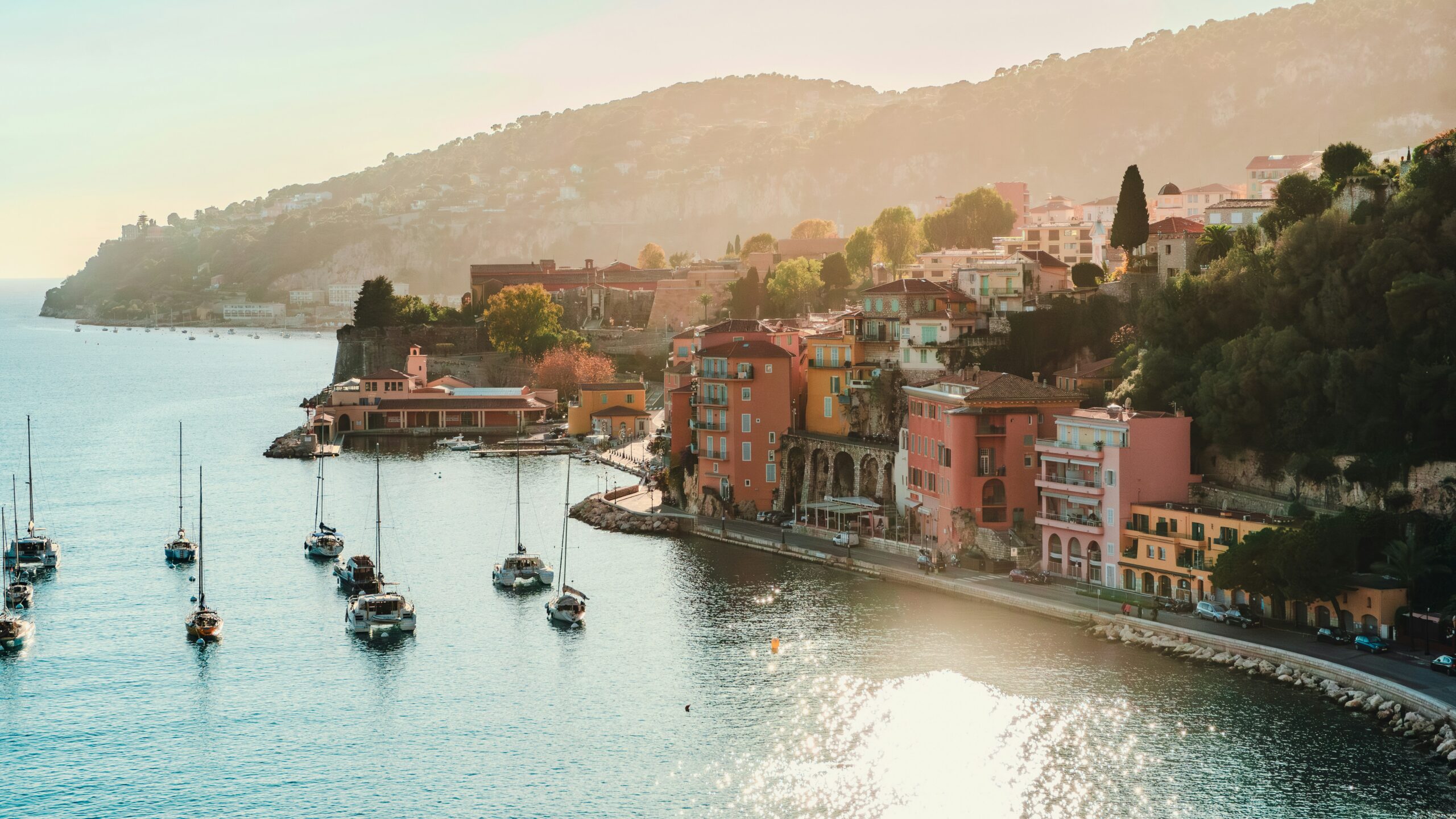 Sunlit view of St. Tropez on the French Riviera with pastel waterfront houses and luxury yachts, capturing the refined resort atmosphere associated with The White Lotus aesthetic.