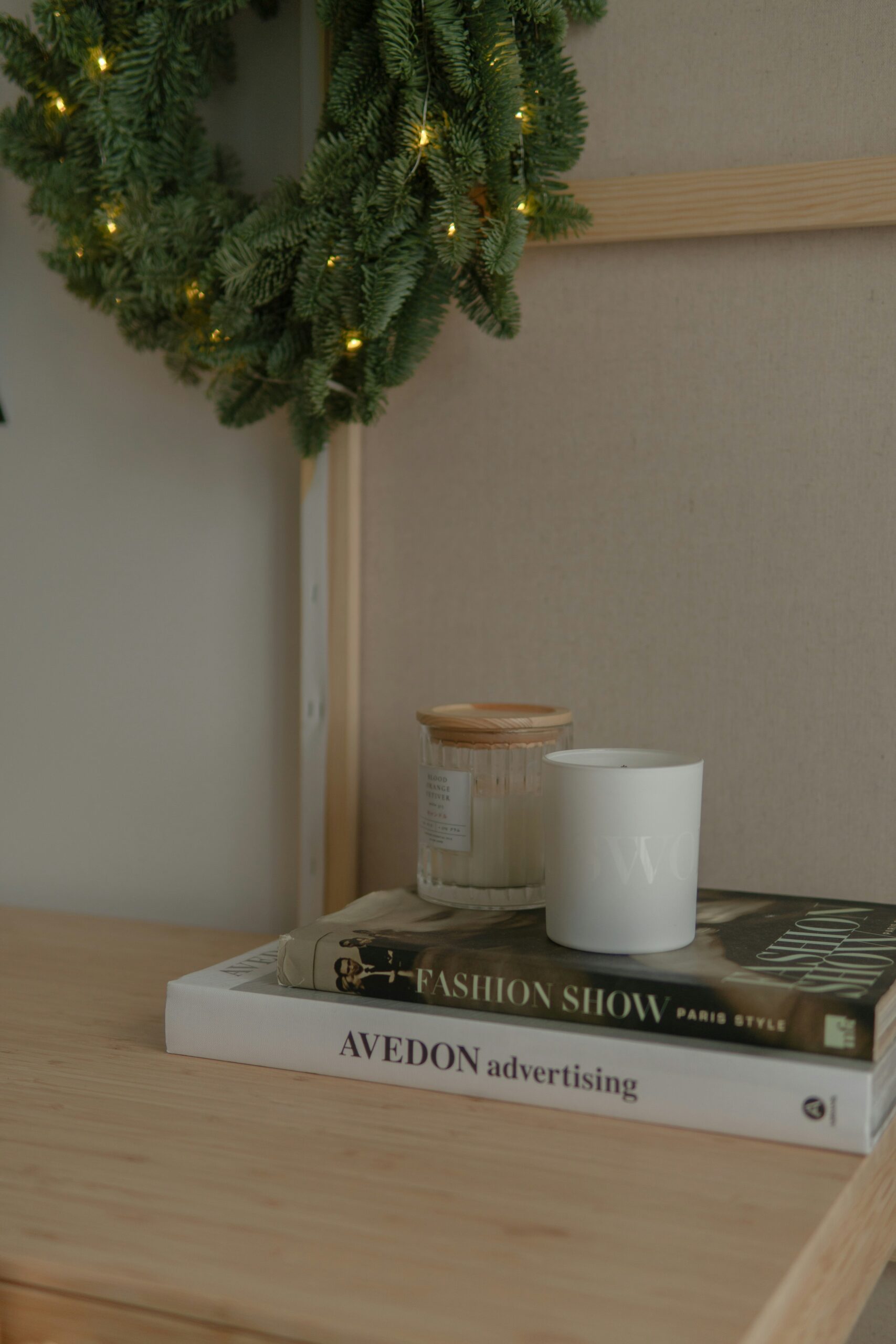 Stack of coffee table fashion books with scented candles on a wooden bedside table creating a cozy home atmosphere